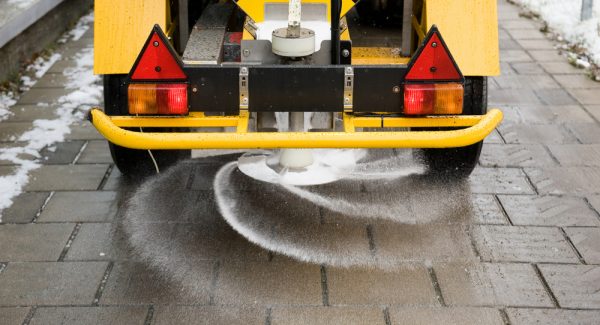 A machine is sprinkling salt on a sidewalk